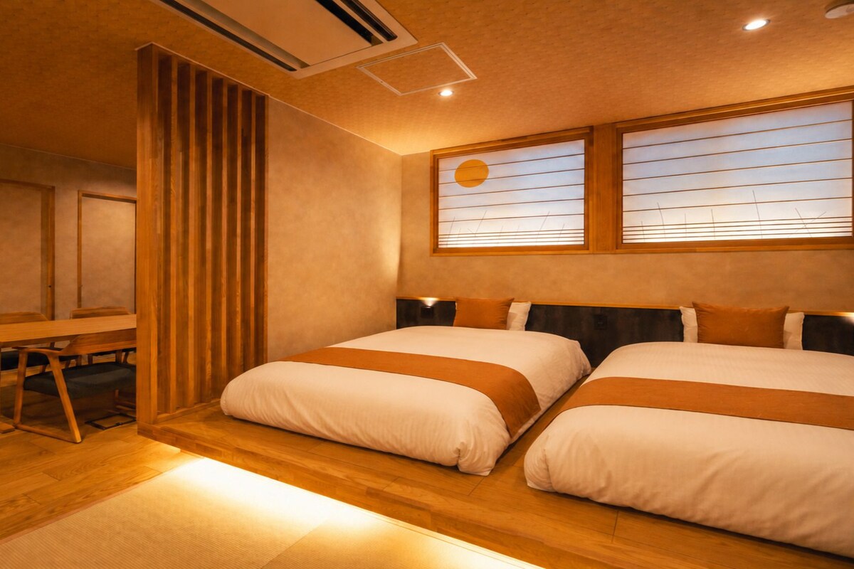 A hotel room with two beds, a wooden desk, and a window with blinds.