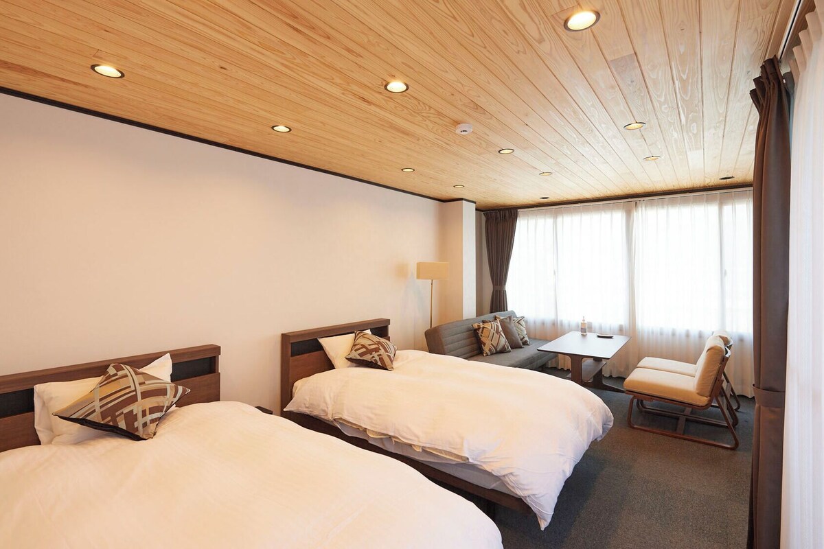 Een hotelkamer met twee bedden, een bank, een kleine tafel en een raam met gordijnen.