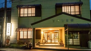 A building with a traditional entrance, a sign with Japanese characters, and a small garden area. - Ubeshimakan (Wakasa)