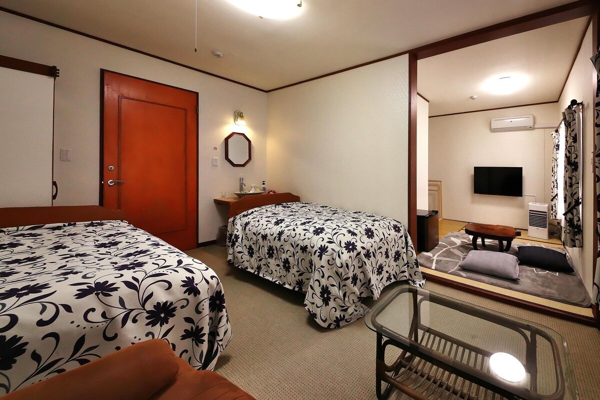 Habitación de hotel con dos camas, una mesita de noche, un espejo, un televisor y aire acondicionado.