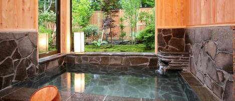 Un jacuzzi con paredes de piedra y una cubierta de madera, rodeado de un jardín y una valla de madera.