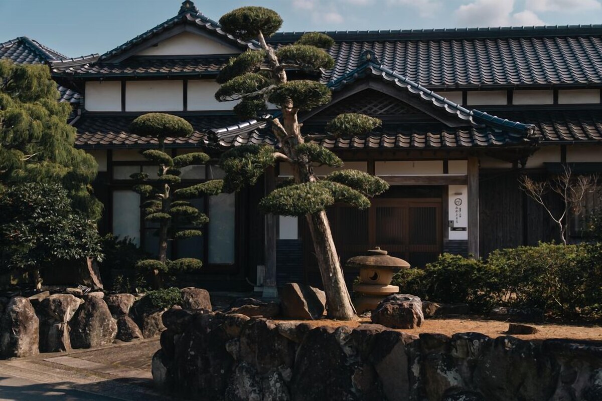 Ein traditionelles japanisches Gebäude mit einem Ziegeldach, Steinlaternen und gepflegten Bonsai-Bäumen.