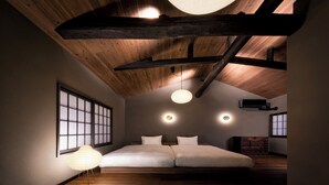 A bedroom with a sloped ceiling, wooden beams, a large bed, and a traditional Japanese-style lamp.