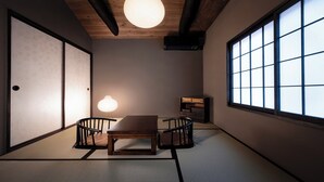 A traditional Japanese room with tatami flooring, a low table, two chairs, a lamp, and a sliding door.