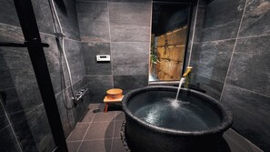 Um banheiro moderno com azulejos escuros, vaso sanitário de madeira, uma banheira grande preta e parede de bambu.