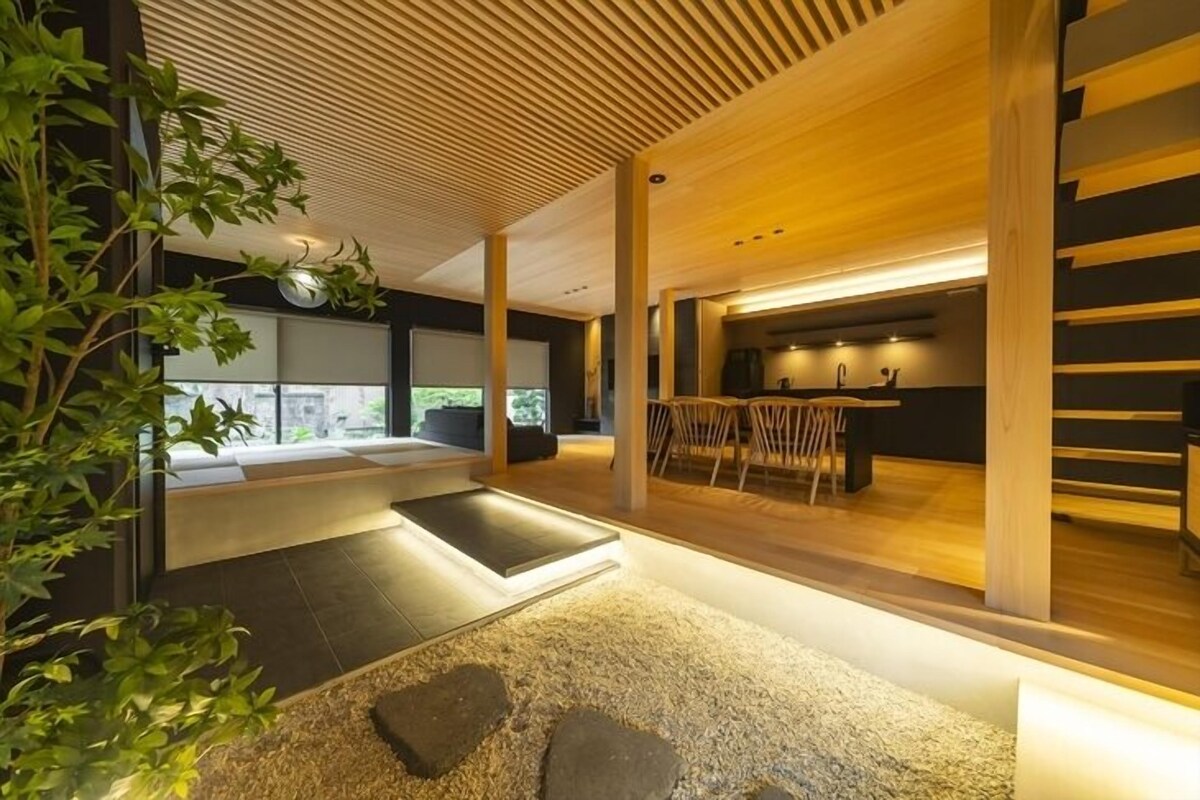 A modern interior with a wooden ceiling, a dining area with chairs and a table, and a seating area with cushions.