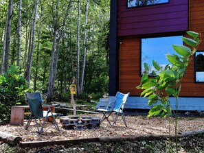 A modern building with a wooden exterior and large windows. There are two folding chairs and a small table in the foreground, surrounded by a forested area. - Green Saso (Kutchan)