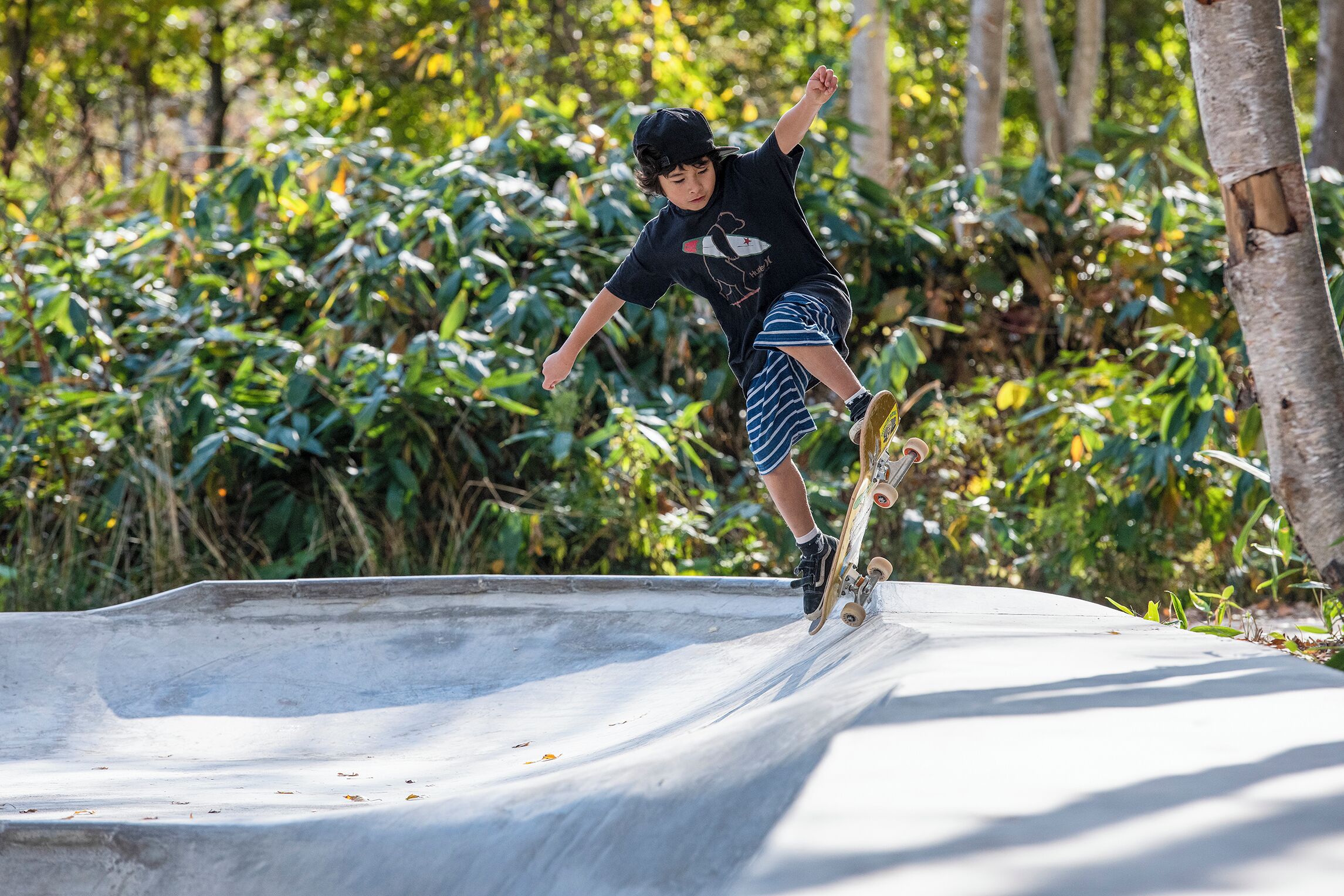 Une personne fait du skateboard sur une rampe en béton, avec de la verdure en arrière-plan.