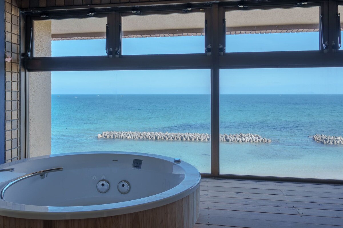 A bathroom with a bathtub, large windows, and a view of the sea.