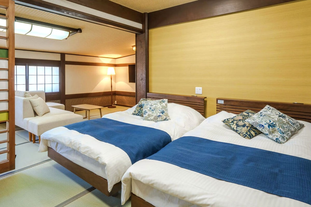 A hotel room with two beds, a sofa, a table, and a traditional Japanese sliding door.