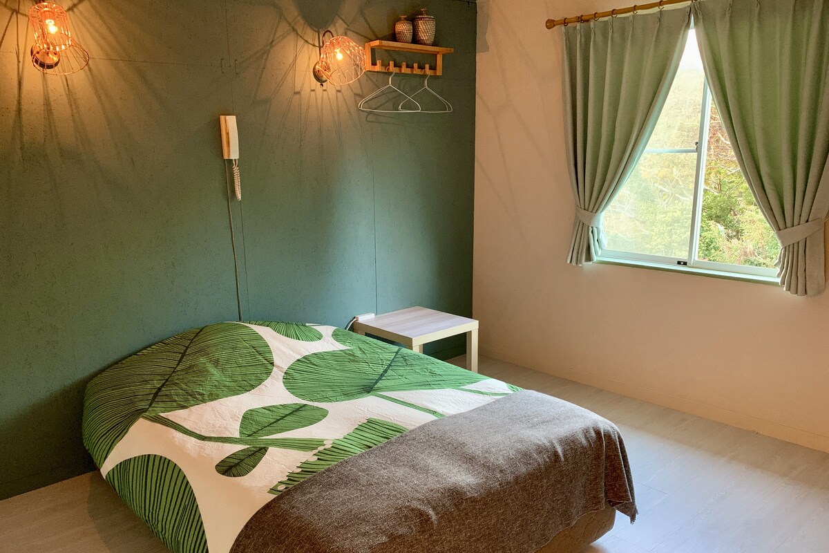 A room with a bed, a bedside table, a wall-mounted light fixture, and a window with curtains.