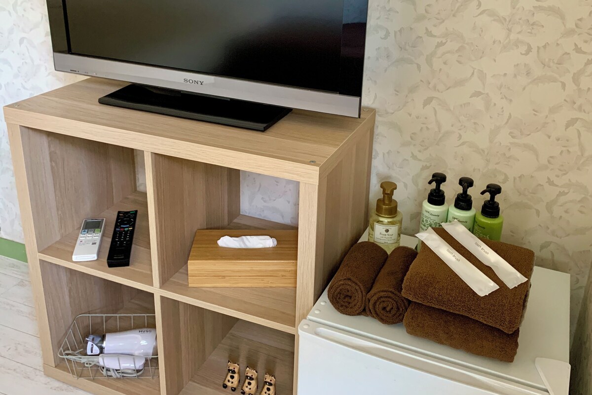 A wooden TV stand with a Sony TV, remote controls, a white box, and toiletries on a white cabinet.