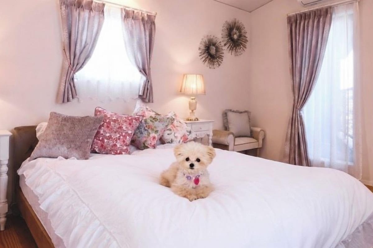 A bedroom with a bed, pillows, a nightstand, a lamp, and a teddy bear.