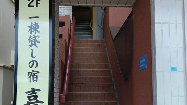 Una escalera que conduce a un segundo piso, con un letrero que indica el número de habitación.