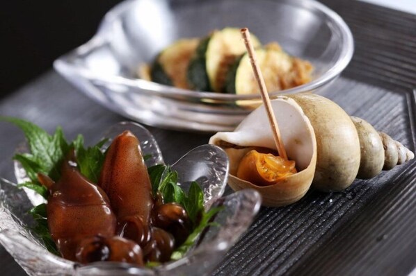 Una mesa de comedor con un cuenco de vidrio que contiene un plato de caracoles, un plato de metal con un guiso de verduras y una concha con una cuchara.