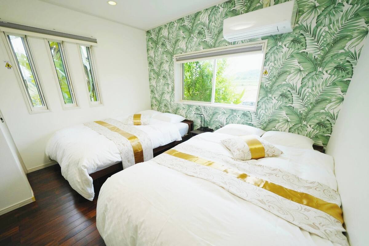 Quarto de hotel com duas camas, janela com vista e papel de parede tropical.