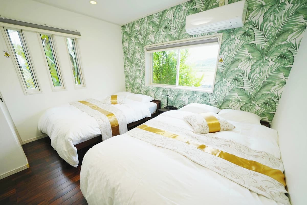 Una habitación de hotel con dos camas, una ventana con vistas y un papel pintado tropical.