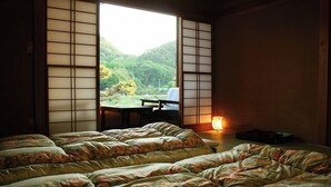 A traditional Japanese room with tatami flooring, a low table, and a bed with floral bedding.