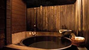 A wooden spa room with a large bathtub, a stone basin, and a wooden bucket.