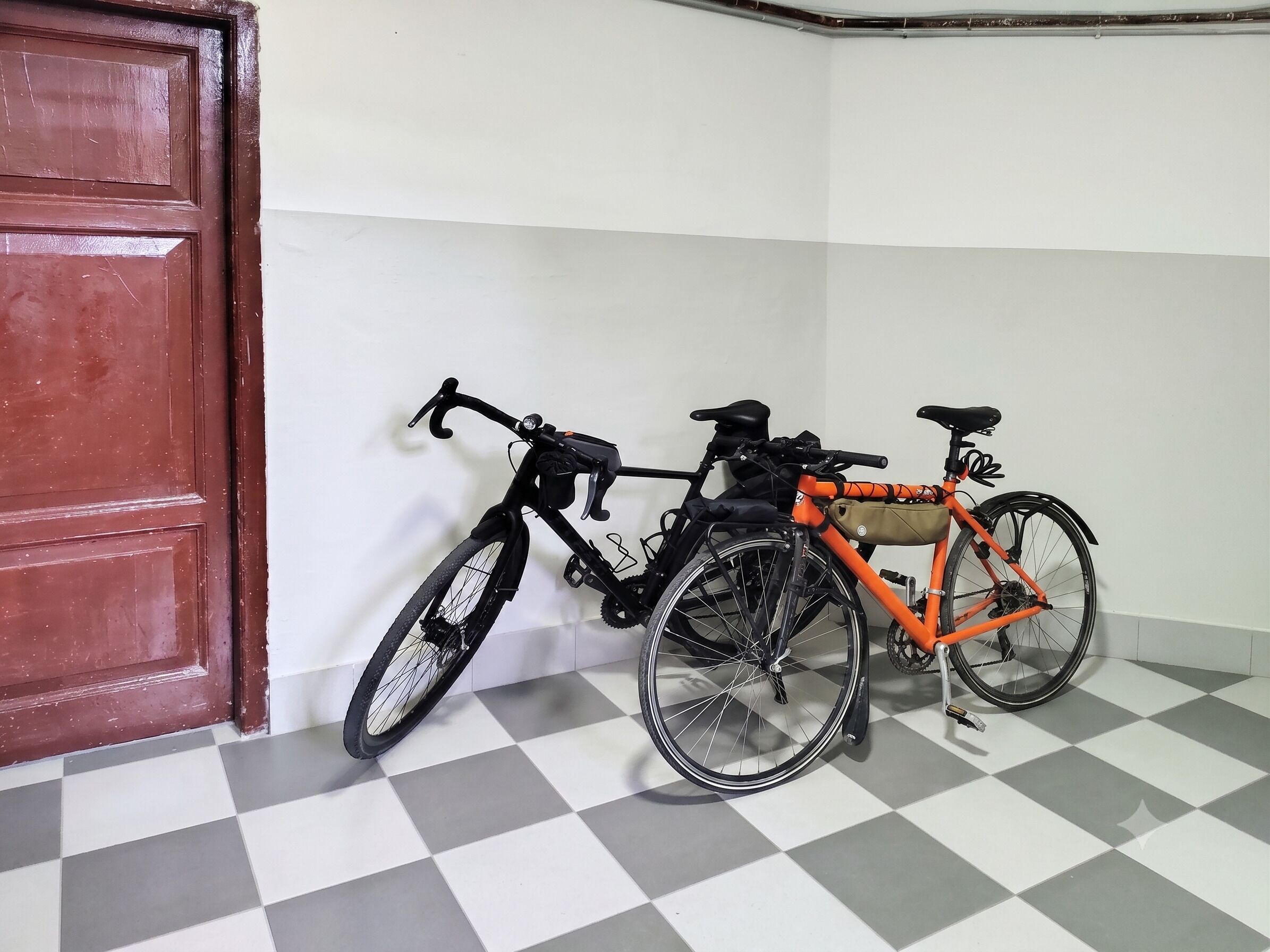 A room with a checkered floor, a red door, and two bicycles leaning against the wall.