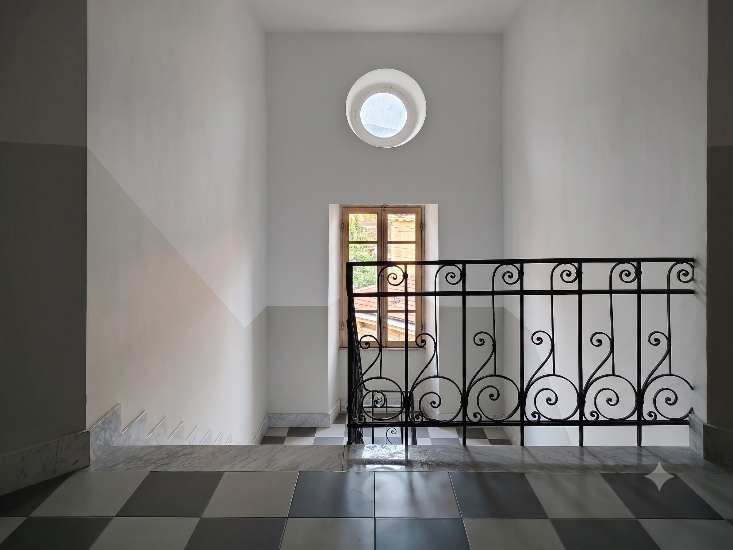 A staircase with a checkered floor, a black wrought iron railing, and a small circular skylight.
