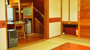 A traditional Japanese room with tatami flooring, a wooden table, a desk with a chair, a small refrigerator, and a staircase leading to another room.