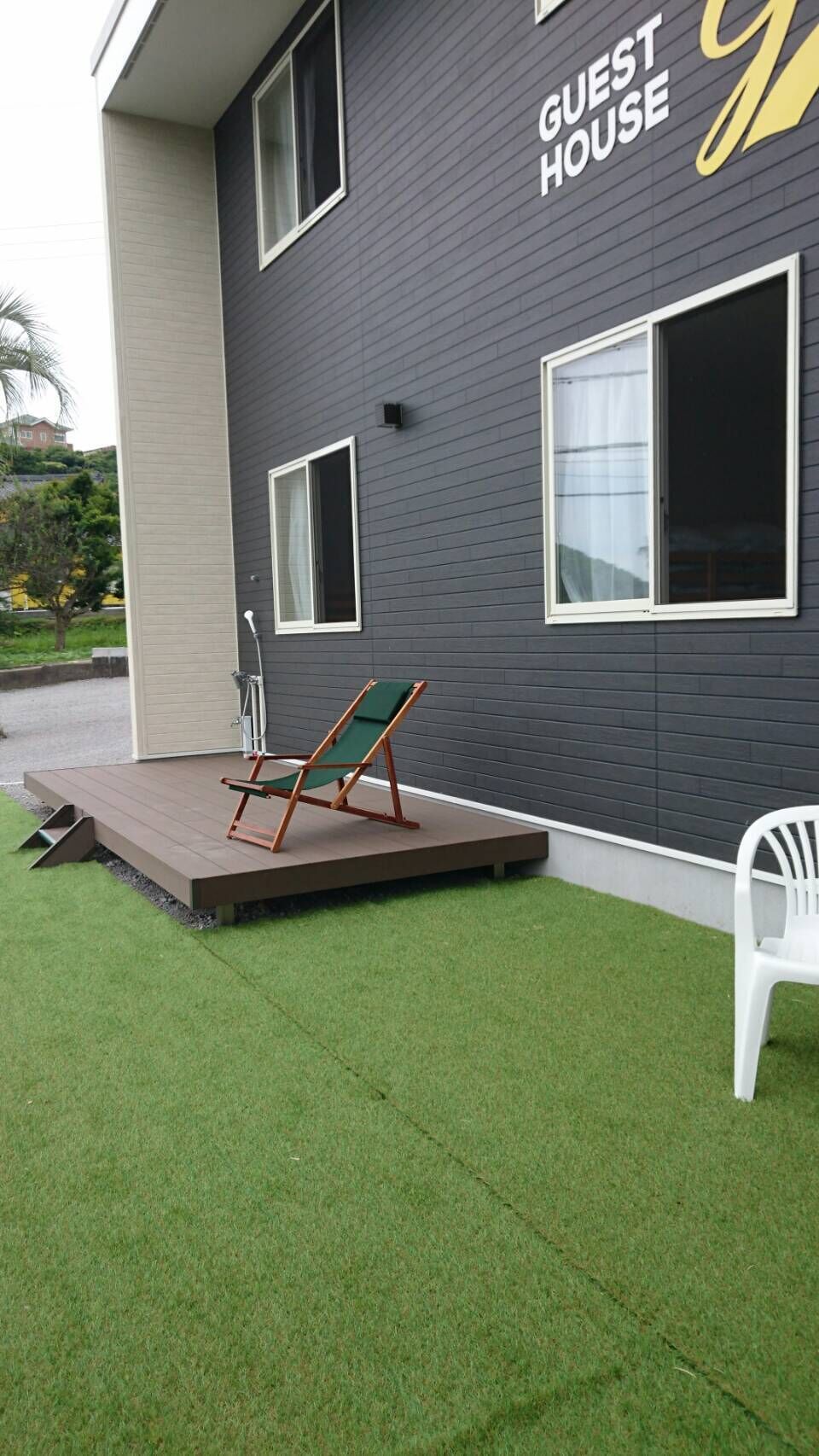 Un edificio moderno con un letrero que dice 'GUEST HOUSE' y un pequeño espacio al aire libre con una silla verde y una blanca.
