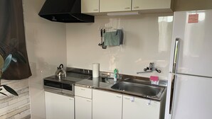 A modern kitchen with white cabinets, a stainless steel sink, a kettle, and a refrigerator.