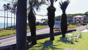 A roadside view with palm trees, a road, and a building with a red roof.