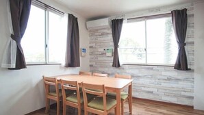 A dining area with a wooden table and chairs, large windows with curtains, and a stone wall.
