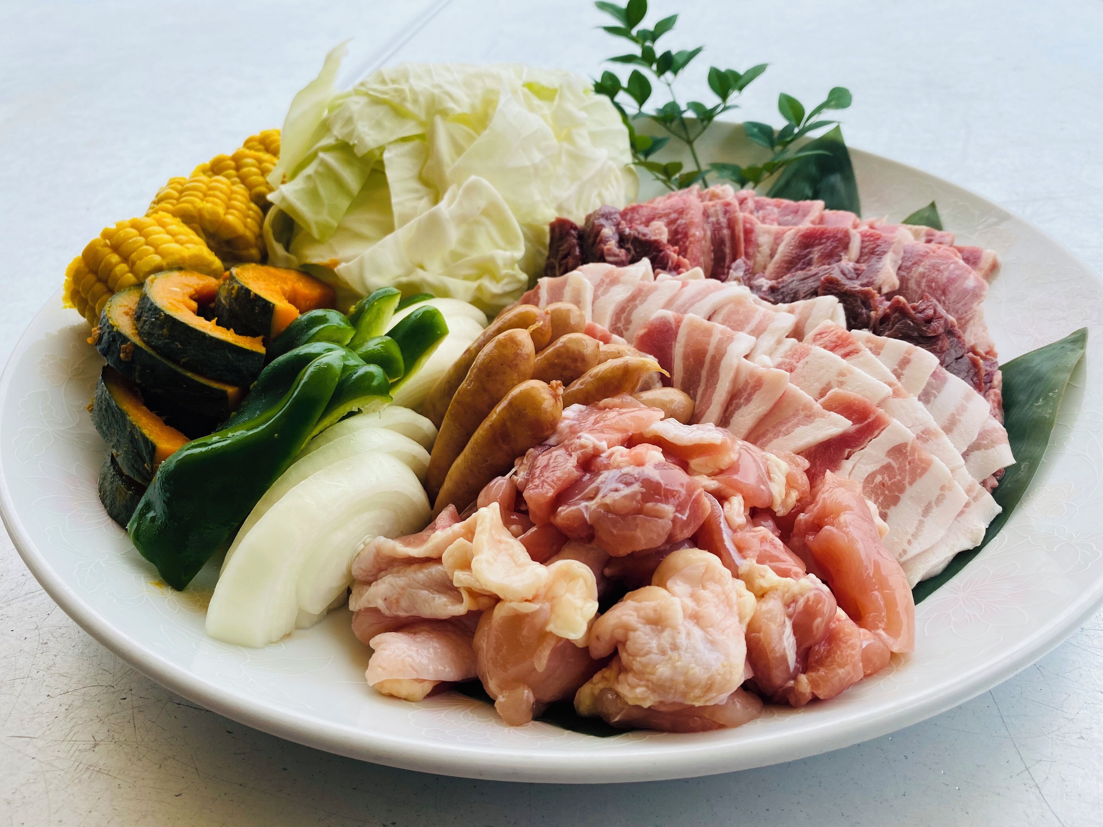 A plate with various raw meats, vegetables, and corn.