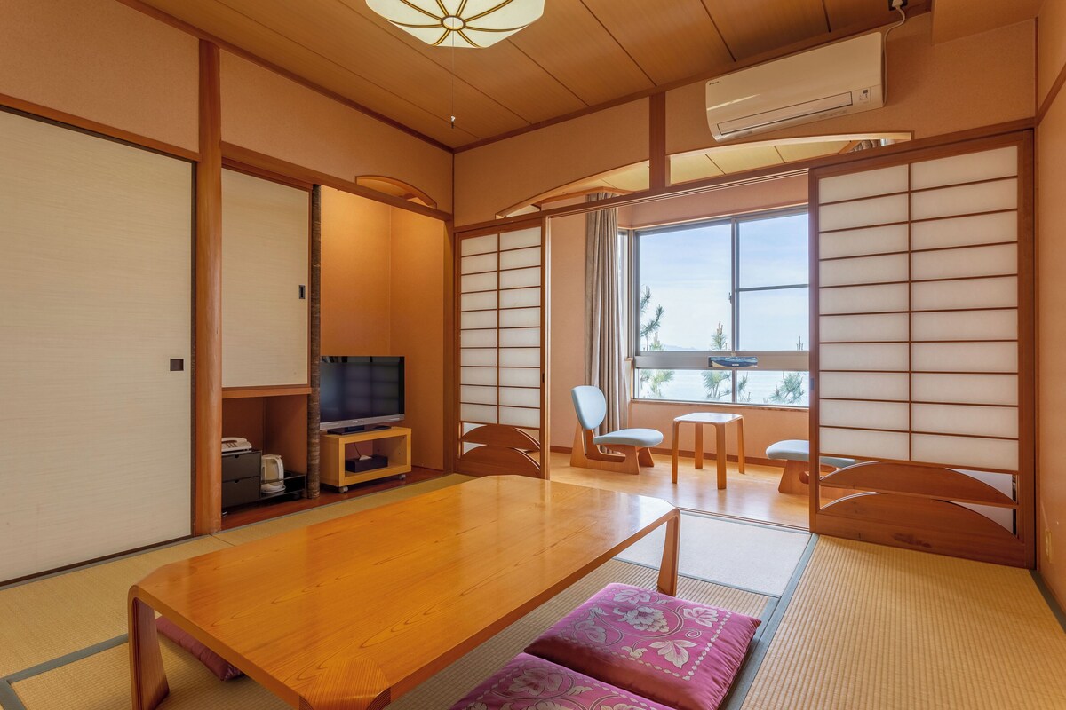 Une pièce de style japonais traditionnel, avec un sol recouvert de tatamis, une table basse, un téléviseur et des portes coulissantes.