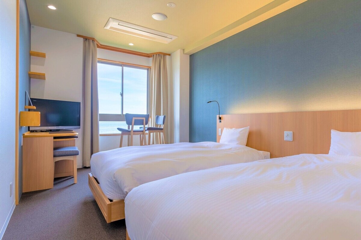 Une chambre d’hôtel avec deux lits, un bureau avec une télévision, une chaise et une fenêtre avec des rideaux.