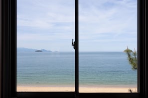Vista a través de una ventana que muestra una playa con aguas tranquilas y islas lejanas.