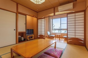 Ein traditioneller japanischer Raum mit Tatami-Böden, einem Holztisch, einem Fernseher und Schiebetüren.