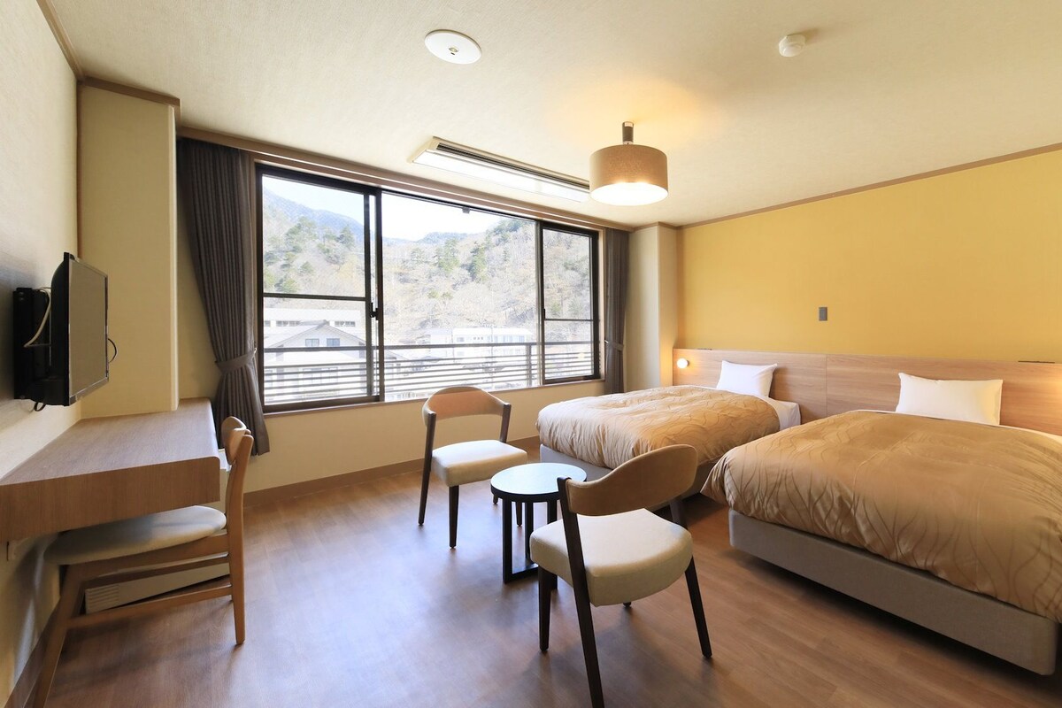 Habitación de hotel con escritorio, dos sillas, cama y televisor.