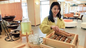 A person arranging food items in a tray, with a beverage dispenser and bowls in the background.