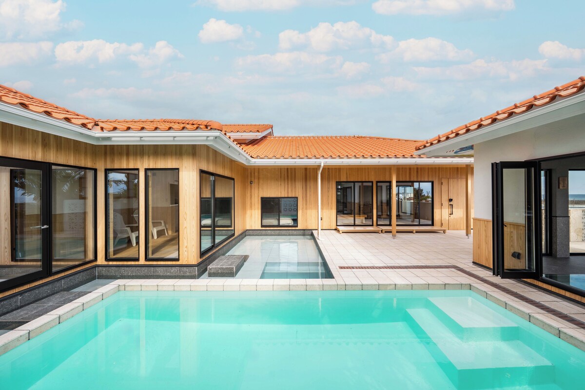 A modern pool area with a clear pool, wooden exterior walls, and large sliding glass doors.
