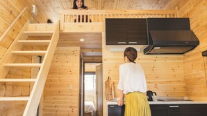 A wooden cabin interior with a kitchen area, a dining space, and a staircase.