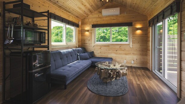 A cozy cabin interior with a wooden ceiling, a sofa, a dining table, and a large window.