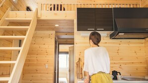 A wooden interior with a kitchen area, a staircase, and a person standing by the counter.
