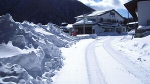 A snow-covered road leading to a building with a sloped roof, surrounded by snowbanks and mountains. - Shinshu Norikura Kogen Onsen Ryokuzansou (Matsumoto)