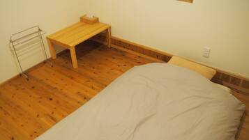 Ein Schlafzimmer mit Holzboden, einem Einzelbett, einem Nachttisch aus Holz, einem kleinen Tisch und einem Fenster.