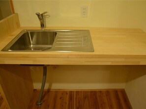 A kitchen with a stainless steel sink, wooden countertop, and a visible plumbing pipe.