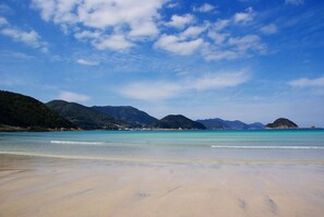 A beach with clear water, sandy shore, and mountains in the background.