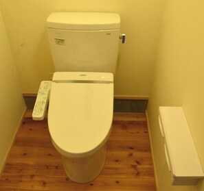 A toilet with a control panel, a wooden floor, and a white wall.