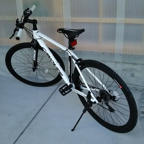 A white bicycle with a black seat and front fork, equipped with a water bottle holder and a rear rack.