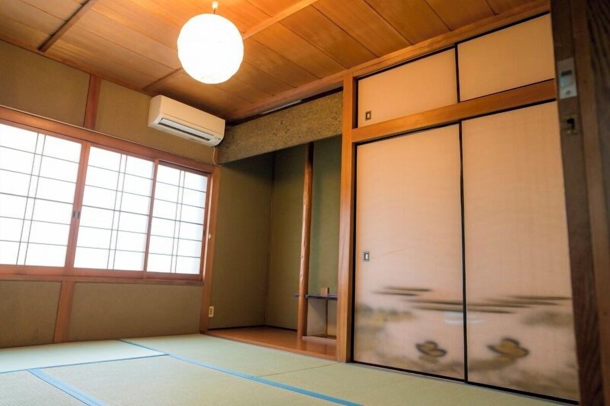 A traditional Japanese room with tatami flooring, sliding doors, and a ceiling fan.
