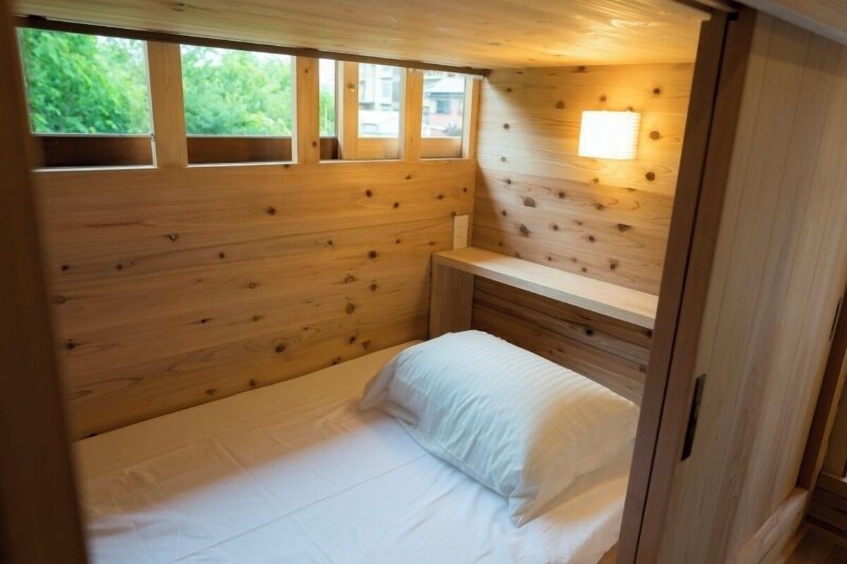 A small, wooden room with a bed, a bench, and a window.
