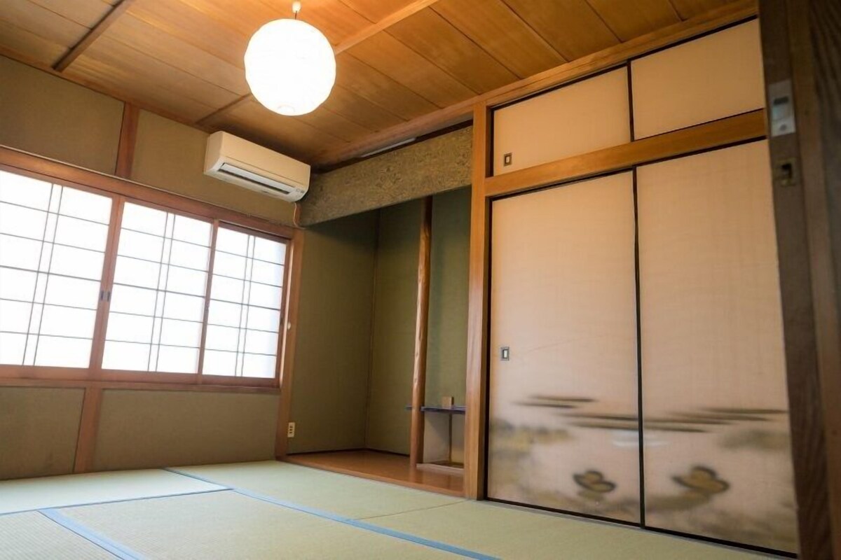 A traditional Japanese room with tatami flooring, sliding doors, and a ceiling fan.